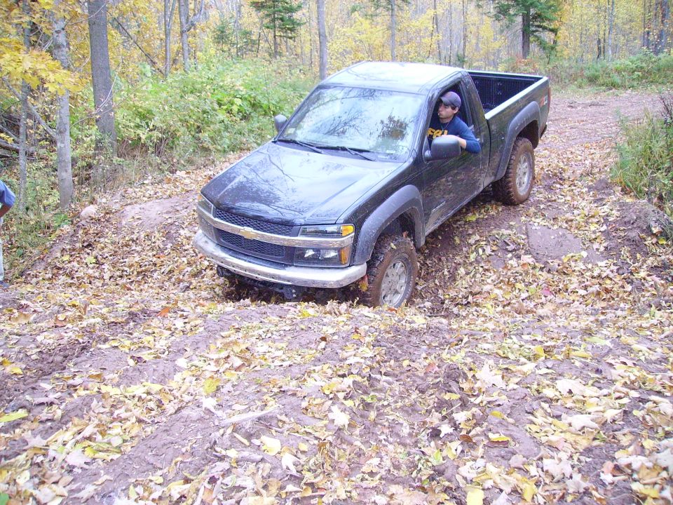 Dark green pickup truck stuck in mud on a dirt path with fallen leaves