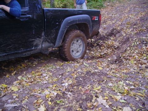 2000 Chevrolet Tahoe - A black pickup truck navigates a muddy, off-road path covered in fallen leaves.