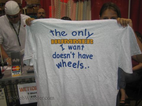 1990 Ford Bronco - woman holds up a gray T-shirt printed "the only HUMMER I want doesn't have wheels.." at a vendor booth with a card-payment sign.