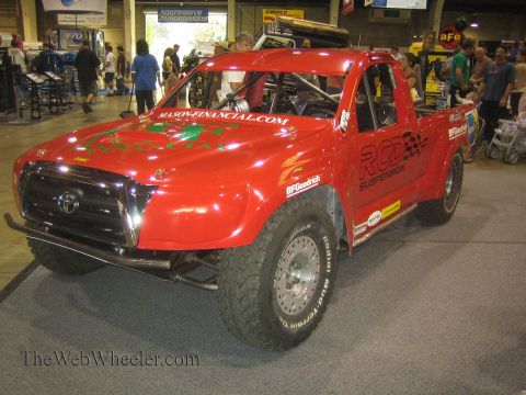 1990 Ford Bronco - red Toyota prerunner race truck with RCD Suspension and BFGoodrich graphics sits on display under indoor lighting as visitors walk past.