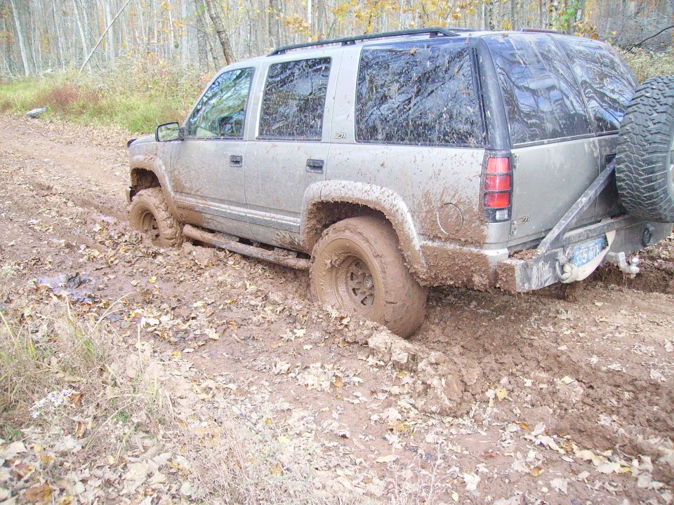 Silver 2000 Chevrolet Tahoe stuck in mud on a dirt road, rear view