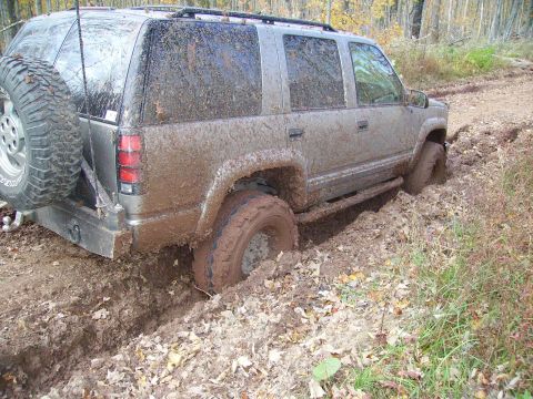 2000 Chevrolet Tahoe - This SUV is deeply stuck in mud on a wooded trail, with its tires submerged.