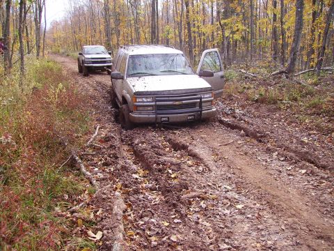 2000 Chevrolet Tahoe - Two SUVs navigate a muddy forest path during autumn, with one vehicle deeply mired.