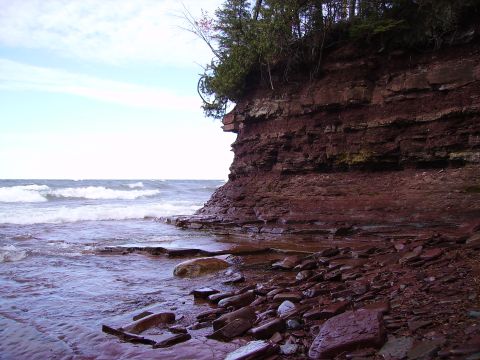 2000 Chevrolet Tahoe - A scenic view of a rocky cliff face meeting the water, with waves lapping at the shore. The image includes a SUPERMOTORS watermark.