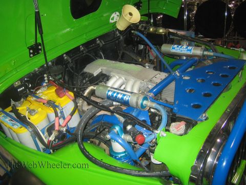 1990 Ford Bronco - engine bay of a green off-road vehicle packed with a V-engine, blue plumbing, King reservoir shocks, batteries and a bypass-shock mounting…