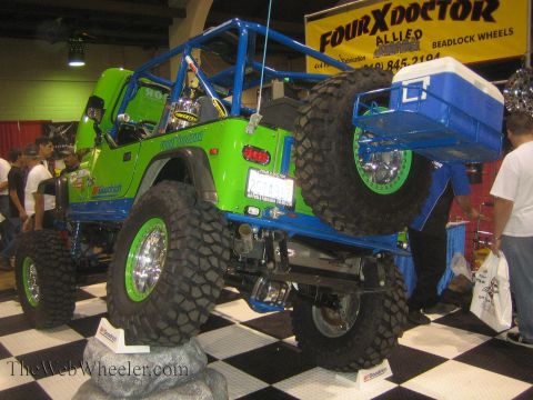 1990 Ford Bronco - Rear view of a green tube-caged Jeep crawler with green beadlock wheels and a blue cooler box mounted to the tube bed, under a Four X Docto…