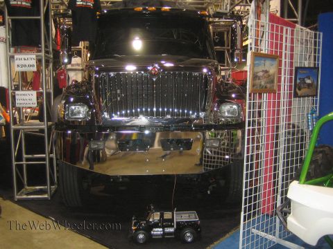 1990 Ford Bronco - chrome-grilled International medium-duty truck looms over the booth with a small radio-control model truck parked on the floor beneath its…