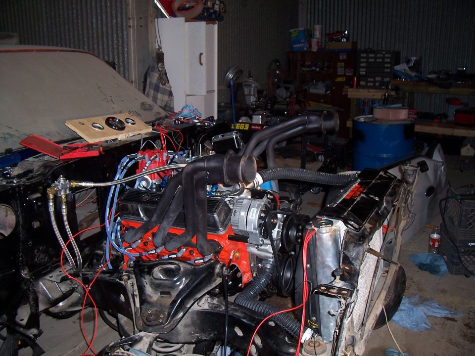 Orange small-block V8 installed in stripped project car with headers and loose radiator