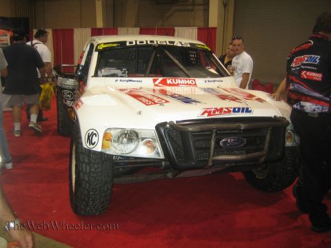 1990 Ford Bronco - white Ford Ranger off-road race truck wearing Amsoil, Kumho and Douglas graphics with a tube front bumper is displayed on red carpet indoor…