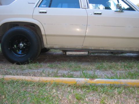 1985 Ford Crown Victoria LTD - The side profile of a tan Ford Crown Victoria reveals its exhaust system and a black aftermarket wheel.