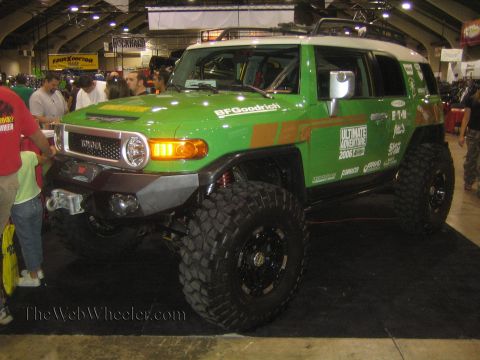 1990 Ford Bronco - Front three-quarter view of a green lifted Toyota FJ Cruiser with a tube bumper, winch and large mud tires at an indoor expo.