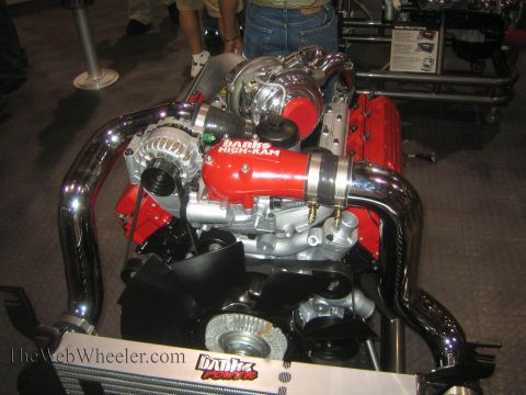 1990 Ford Bronco - red Banks Power diesel V8 engine fitted with a turbocharger and polished chrome intake piping sits on a display stand.