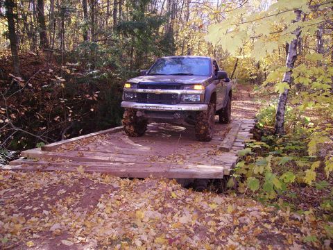 2000 Chevrolet Tahoe - A lifted Chevrolet Colorado navigates a narrow wooden bridge surrounded by fall foliage.