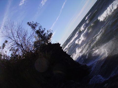 2000 Chevrolet Tahoe - Waves crash violently against a rocky shore under a bright blue sky with wispy clouds.