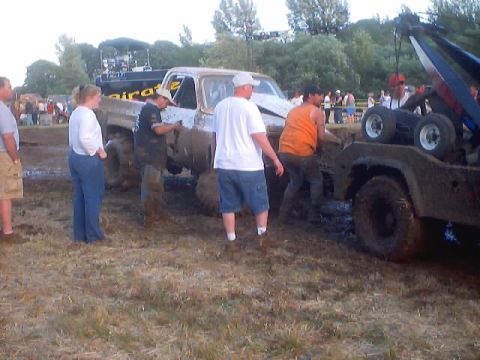 1976 Ford F-100 - A muddy 1976 Ford F-100 pickup truck is being pulled out of the mud by a tow truck during an event.