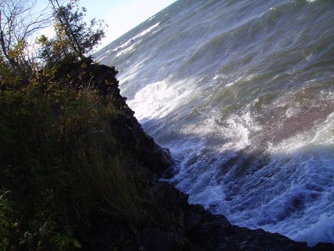 2000 Chevrolet Tahoe - Waves crash against a rocky shoreline under a bright sky, with vegetation on the left.