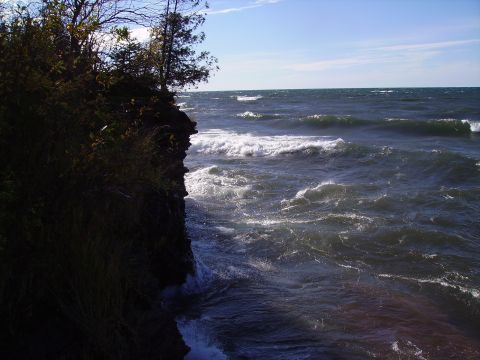 2000 Chevrolet Tahoe - Waves surge against a rocky shore, with trees visible on the cliff edge.