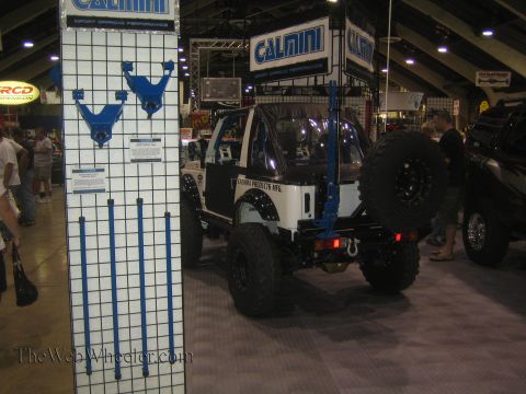 1990 Ford Bronco - white lifted hardtop 4x4 with rear spare sits at the Calmini Products booth next to a blue suspension-parts display at an expo.