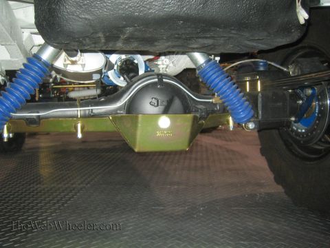 1990 Ford Bronco - Underbody view of a vehicle's rear axle fitted with a gold differential skid plate and blue coil springs over a checkerplate floor.