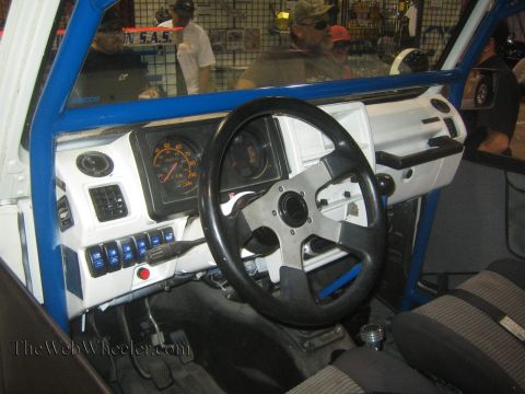 1990 Ford Bronco - Interior of a white off-road 4x4 with a blue roll cage, white dash, large gauge and a four-spoke aftermarket steering wheel.