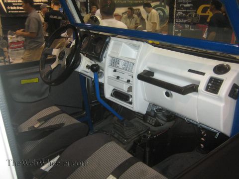 1990 Ford Bronco - Interior of a white off-road 4x4 with a blue roll bar, white dashboard, aftermarket gauge panel and gray cloth seats.