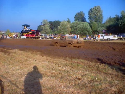1976 Ford F-100 - A 1976 Ford F-100 navigates a muddy track during a competition, with spectators and a radio stage visible.
