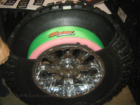 1990 Ford Bronco - off-road tire mounted on a chrome wheel is shown with green and pink Staun foam tire inserts at a product display.