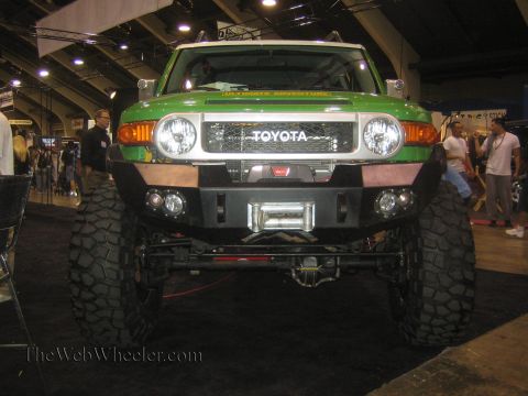 1990 Ford Bronco - green lifted Toyota FJ Cruiser sits on large mud tires with a winch front bumper at an indoor expo.