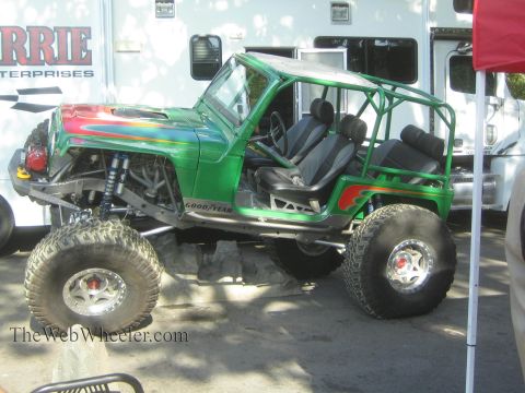 1990 Ford Bronco - green tube-chassis Jeep-bodied rock buggy with caged interior sits on large tires next to a Currie Enterprises trailer.