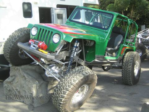 1990 Ford Bronco - green caged Jeep rock crawler on big tires flexes over a boulder, showing its winch, coilovers, and solid axle.
