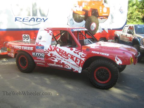 1990 Ford Bronco - red and white Skyjacker and Toyo Tires sponsored off-road race truck number 99 sits on display before a backdrop banner.