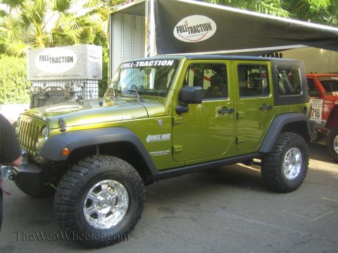 1990 Ford Bronco - green four-door Jeep Wrangler Unlimited on a lift and chrome wheels is displayed at a Full-Traction Suspension booth.