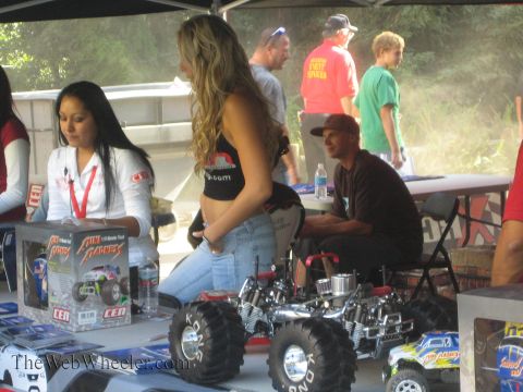 1990 Ford Bronco - People gather at a vendor booth where nitro RC monster trucks and CEN-branded boxes are displayed on a table under a tent.