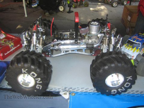 1990 Ford Bronco - Top-down view of a chrome RC monster truck chassis fitted with a nitro engine and large KONG-branded tires on a workbench.