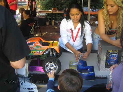 1990 Ford Bronco - Staff and a child gather around an orange CEN radio-controlled monster truck displayed on a table at an outdoor booth.