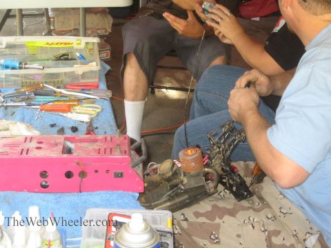 1990 Ford Bronco - Hobbyists work on a disassembled nitro RC engine surrounded by screwdrivers, a pink chassis, and aerosol cans on the ground.