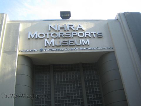 1990 Ford Bronco - metal lettered facade of the NHRA Motorsports Museum, presented by the Automobile Club of Southern California, against blue sky.