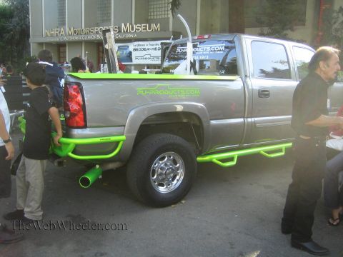 1990 Ford Bronco - silver crew-cab pickup with green PU-Products.com graphics and tubular step bars is displayed outside the NHRA Motorsports Museum.