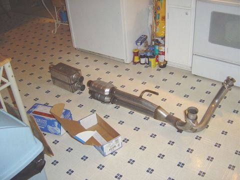 1986 Ford Bronco - A stainless steel exhaust system mockup laid out on a kitchen floor, including a muffler, catalytic converter, and a curved exhaust pipe wi…