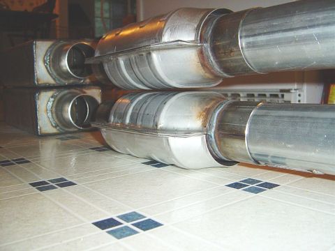 1986 Ford Bronco - A mockup of stainless steel exhaust components including catalytic converters, mufflers, and connecting pipes laid out on a tiled kitchen f…