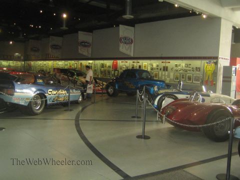 1990 Ford Bronco - Several vintage dragsters and race cars are arrayed on a polished museum floor beneath an NHRA banner and wall exhibits.