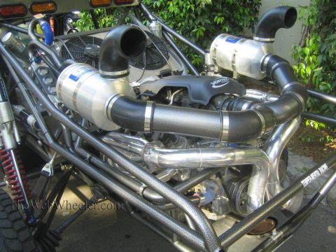 1990 Ford Bronco - mid-engine bay of a tube-chassis off-road buggy shows twin canister air filters, polished intake tubing and a cooling fan.