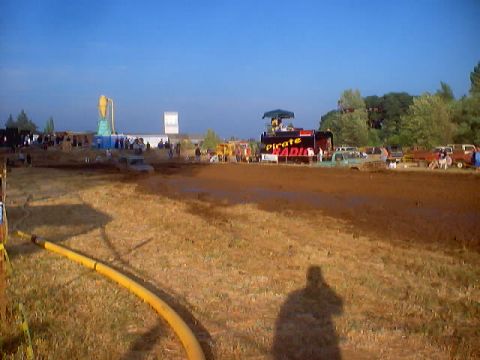 1976 Ford F-100 - A muddy field event with spectators and vehicles, a 'PIRATE RADIO' stage under a clear blue sky.