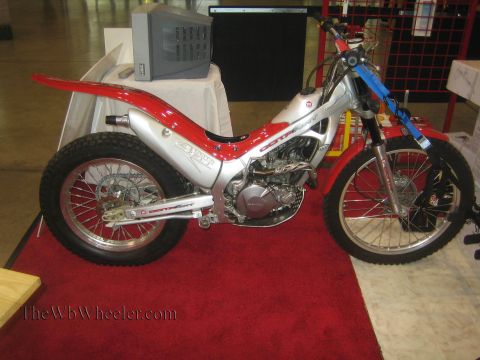 1990 Ford Bronco - red and silver Montesa trials motorcycle with knobby tires sits on a red display carpet at an indoor show.