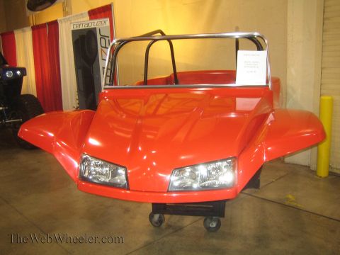 1990 Ford Bronco - red fiberglass-bodied dune buggy with a chrome roll bar sits on casters at an indoor display in front of a curtain.