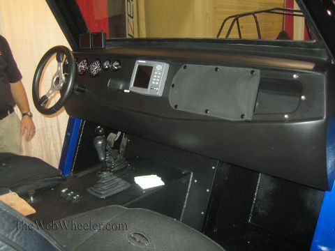 1990 Ford Bronco - Interior of a black-paneled off-road vehicle showing a small steering wheel, gauges, a display screen, shifter and floor-mounted controls.