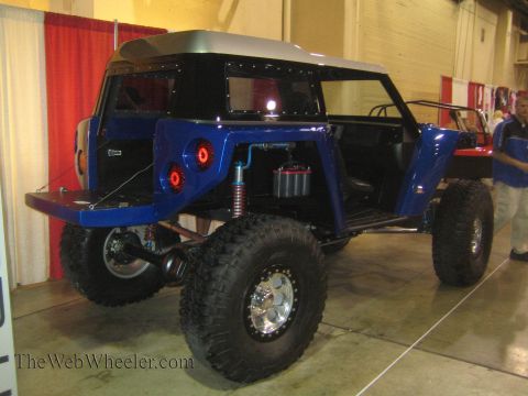 1990 Ford Bronco - Rear three-quarter view of a blue off-road buggy showing its coilover shocks, fuel cell and beadlock wheels at an indoor display.
