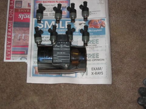 1991 Ford Bronco - Eight fuel injectors and a chrome fuel rail are laid out on top of newspapers.