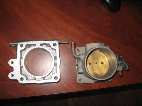1991 Ford Bronco - Two throttle body parts are laid out on a wooden desk.