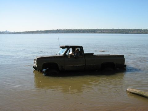 1990 Ford Bronco - A pickup truck navigates through a body of water under a clear blue sky.